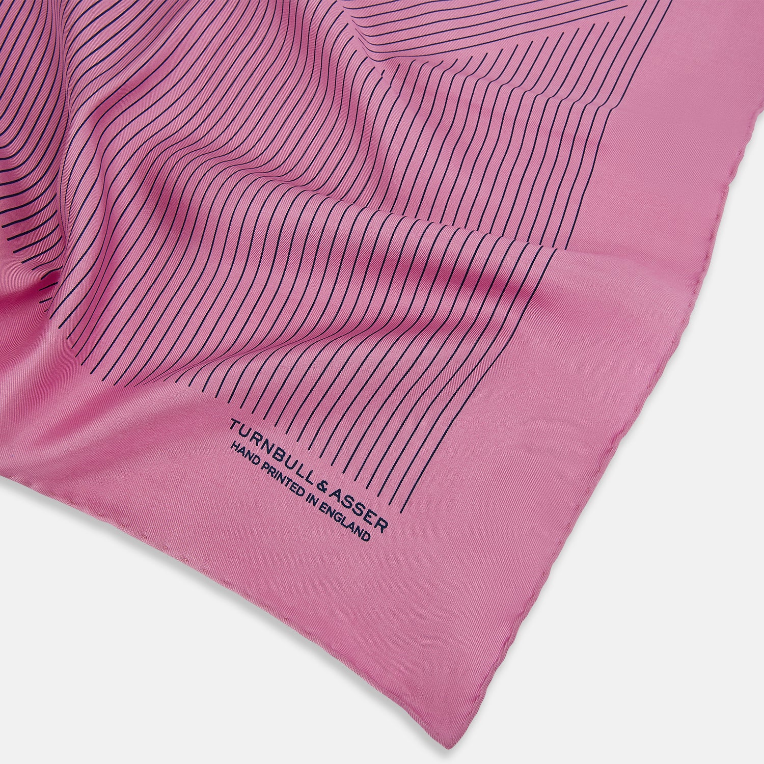 View 2 of product The Turnbull & Asser Pink Stripe Silk Pocket Square features thin vertical navy stripes and "TURNBULL & ASSER HAND PRINTED IN ENGLAND" in the bottom right corner, with one corner stylishly folded over.