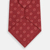 View 3 of product The Turnbull & Asser Red Medallion Silk Tie features a rolled-up red silk design with a repeating geometric pattern of small white circles and cross motifs on a plain white background.