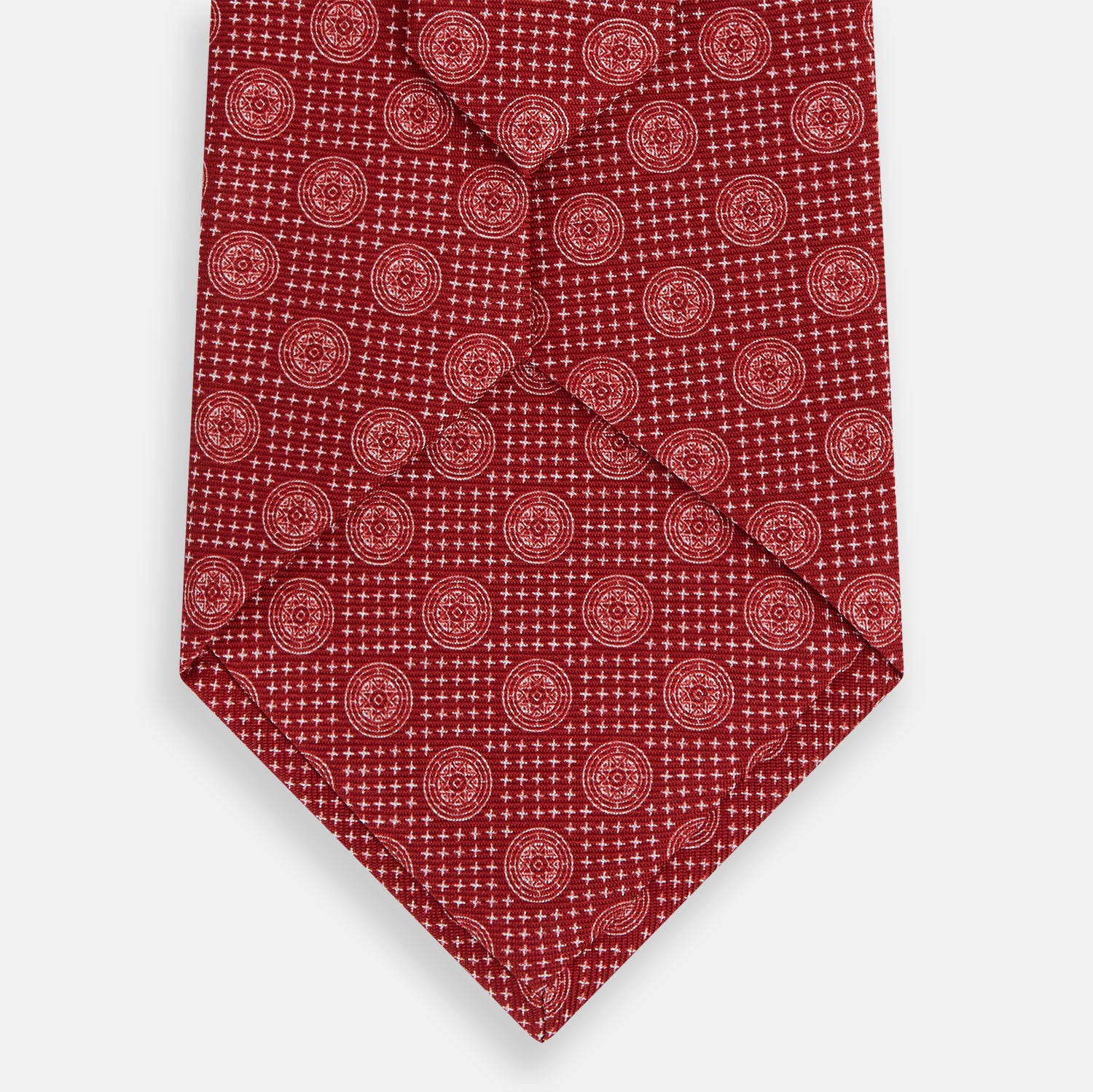 View 3 of product The Turnbull & Asser Red Medallion Silk Tie features a rolled-up red silk design with a repeating geometric pattern of small white circles and cross motifs on a plain white background.