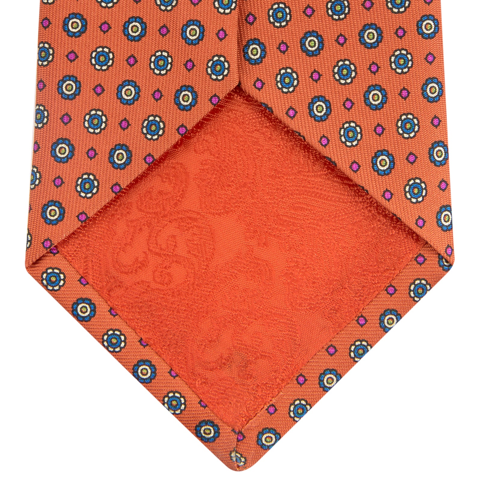 View 4 of product The Great Gatsby Orange Printed Silk Tie by Turnbull & Asser, from the Legends collection, features a repeating pattern of small blue, white, and yellow floral motifs—an ideal summer accessory—shown rolled on a white background.