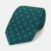 View 1 of product The Forest Green Medallion Silk Tie by Turnbull & Asser showcases a refined medallion pattern, offering an elegant, textured appearance. The tie is neatly rolled and displayed on a plain white background.