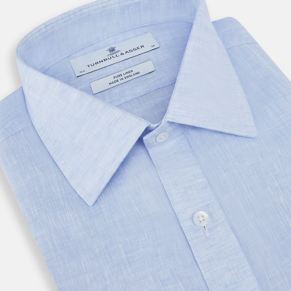 The Turnbull & Asser Pale Blue Linen Mayfair Shirt features a collar, front pocket, and white buttons. This long-sleeve shirt is displayed on a white background.