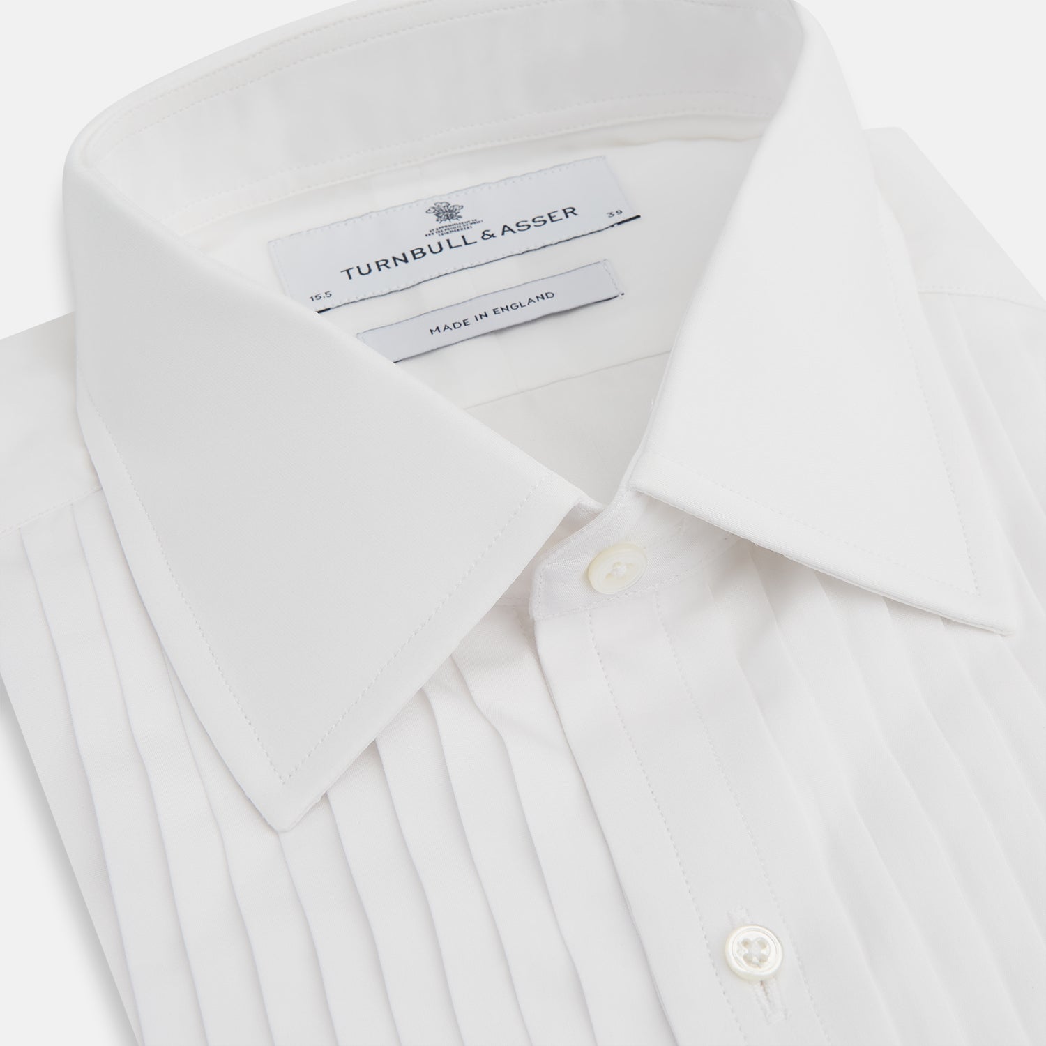 View 2 of product The Turnbull & Asser White Pleated Cotton Dress Shirt features a T&A collar, pleated front, double cuffs, and a button-down front, shown laid flat against a white background.