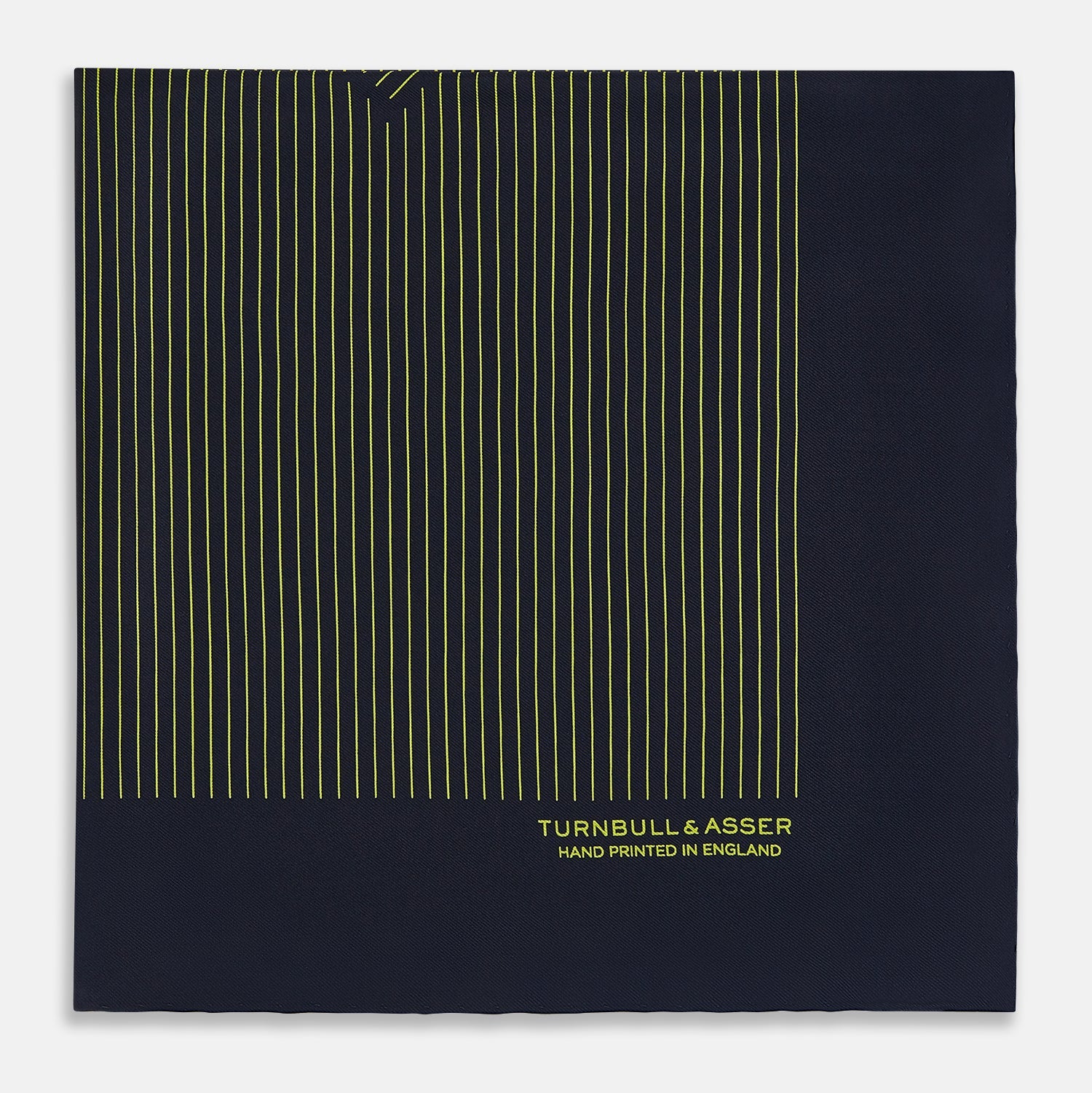 View 4 of product Turnbull & Asser Navy and Yellow Stripe Silk Pocket Square features hand-rolled edges, striped pattern, and "Turnbull & Asser Hand Printed in England" text in yellow on the bottom right corner.