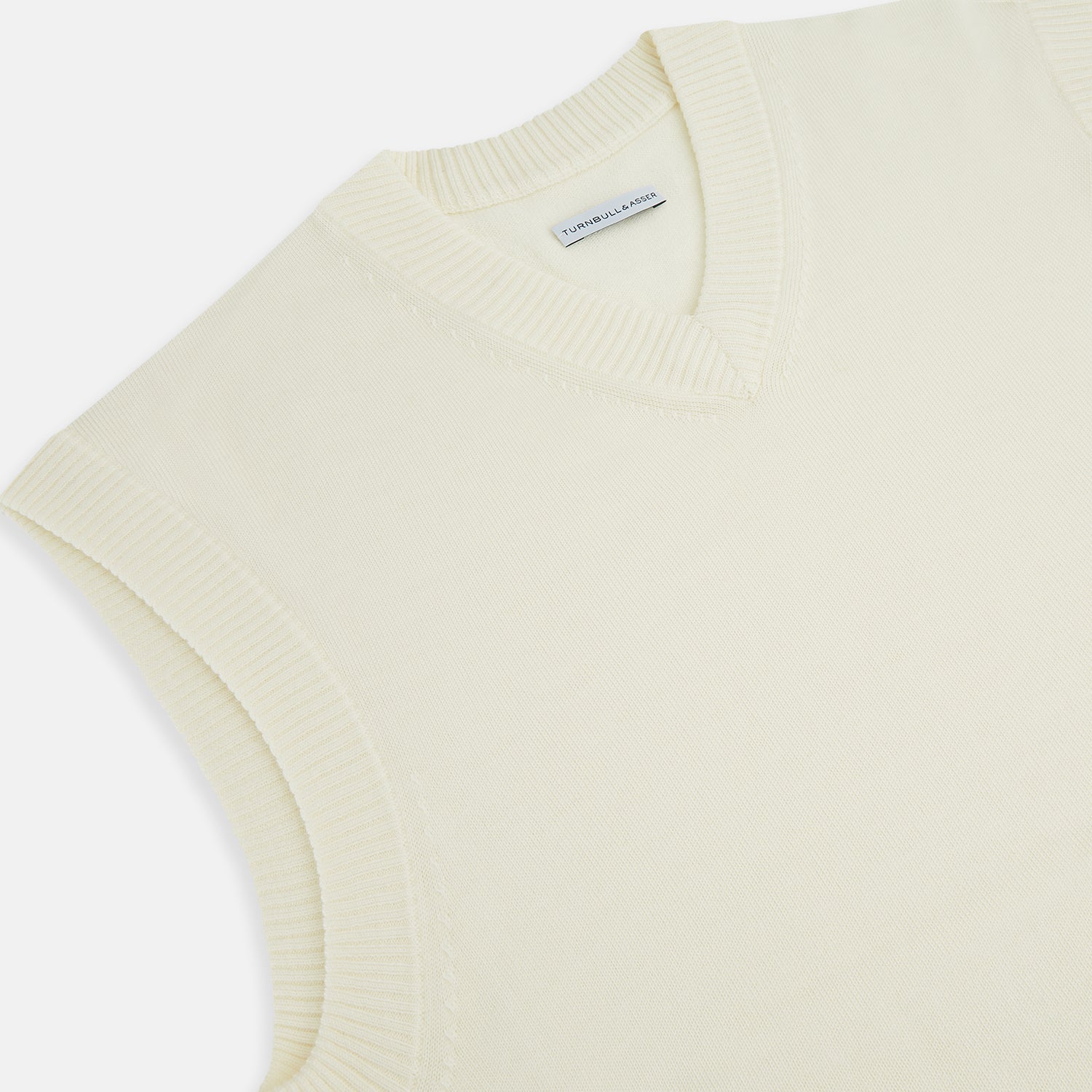 View 2 of product The Ecru Fine Merino V-Neck Vest by Turnbull & Asser is a sleeveless gentleman’s sweater with ribbed edges in cream knit, shown against a plain white background.