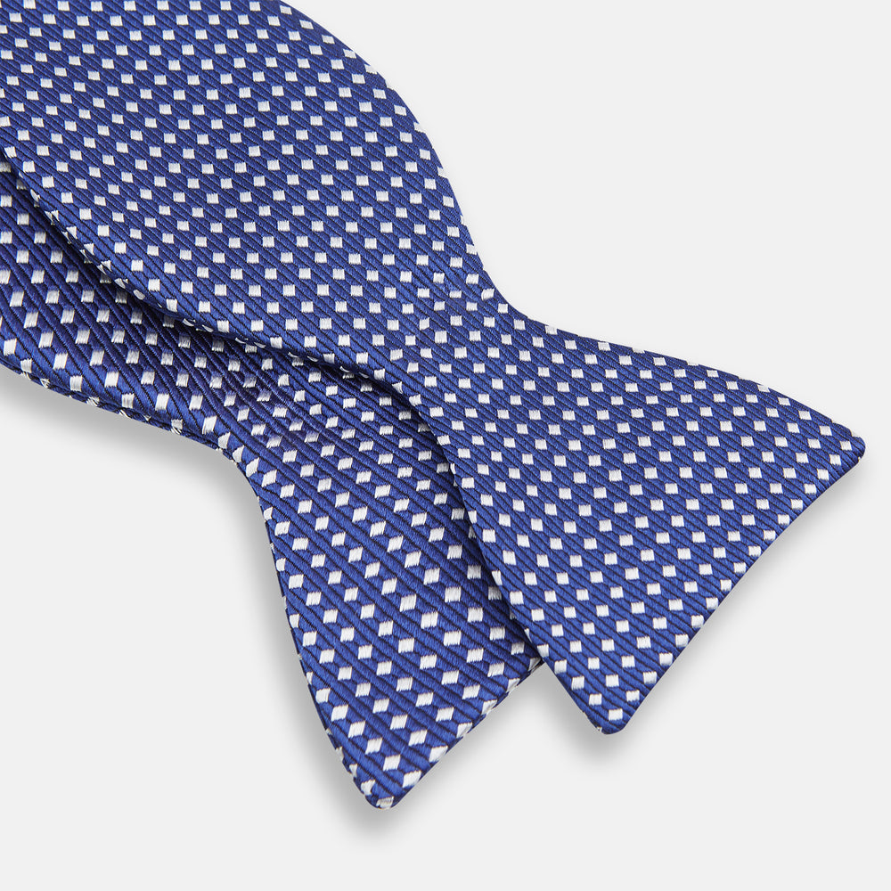 The Turnbull & Asser Blue and White Diamond Silk Bow Tie features a repeating pattern of small white diamonds and vertical ribbing, making it perfect for formalwear. Displayed on a white background.