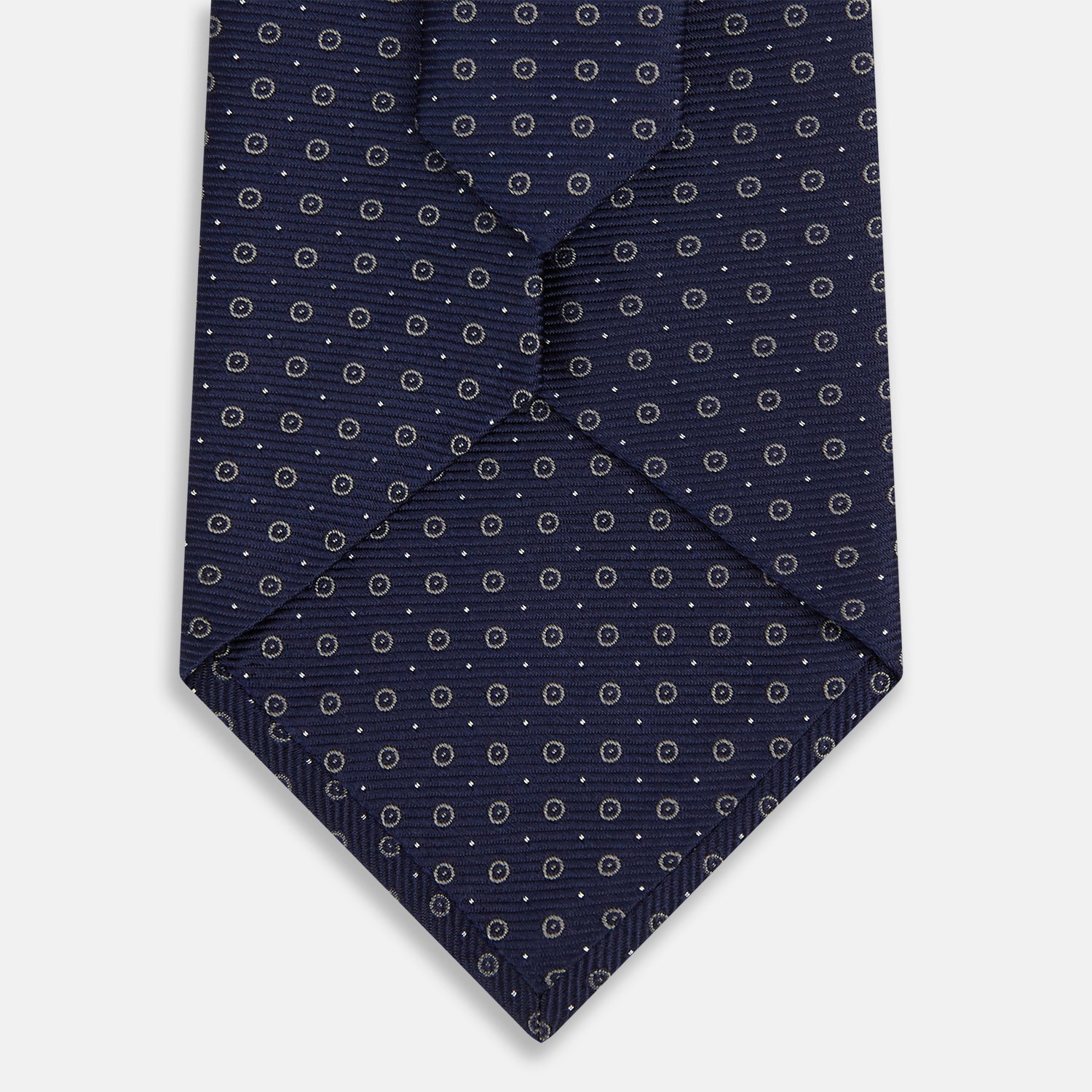 View 3 of product The Turnbull & Asser Navy and Grey Circle Silk Tie, featuring a refined pattern of evenly spaced circles, is elegantly displayed rolled up on a white background—an excellent option for modern office wear.