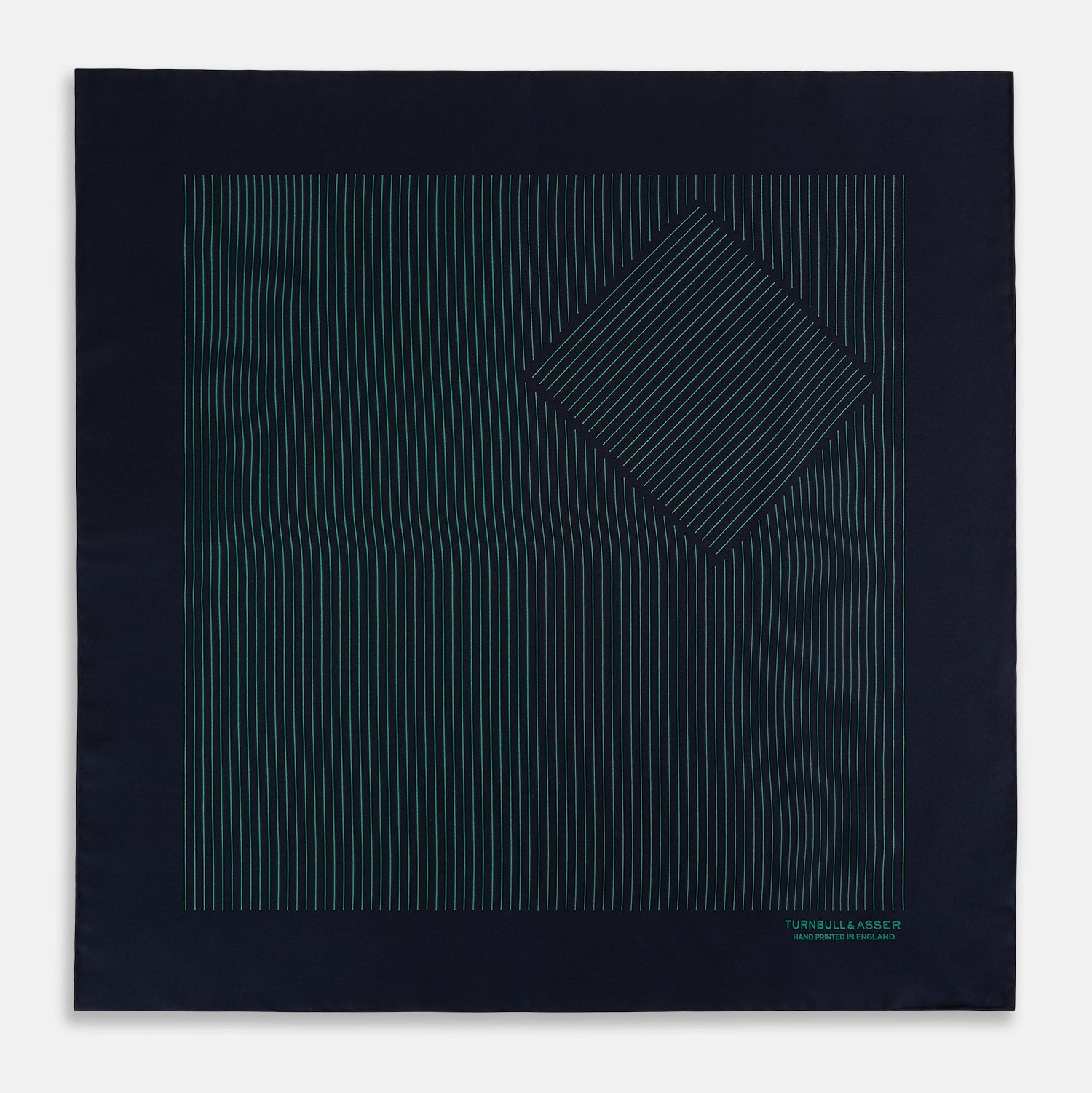 View 4 of product The Turnbull & Asser Navy and Hunter Green Stripe Silk Pocket Square features thin green stripes, hand-rolled edges, and "TURNBULL & ASSER HAND PRINTED IN ENGLAND" in green on the bottom right corner.