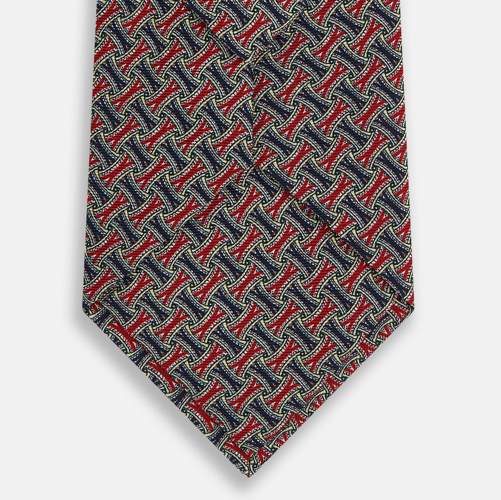 A close-up of the Turnbull & Asser Red and Navy Weave Patterned Silk Tie, showcasing its geometric design in red, blue, white, and yellow on a white background.