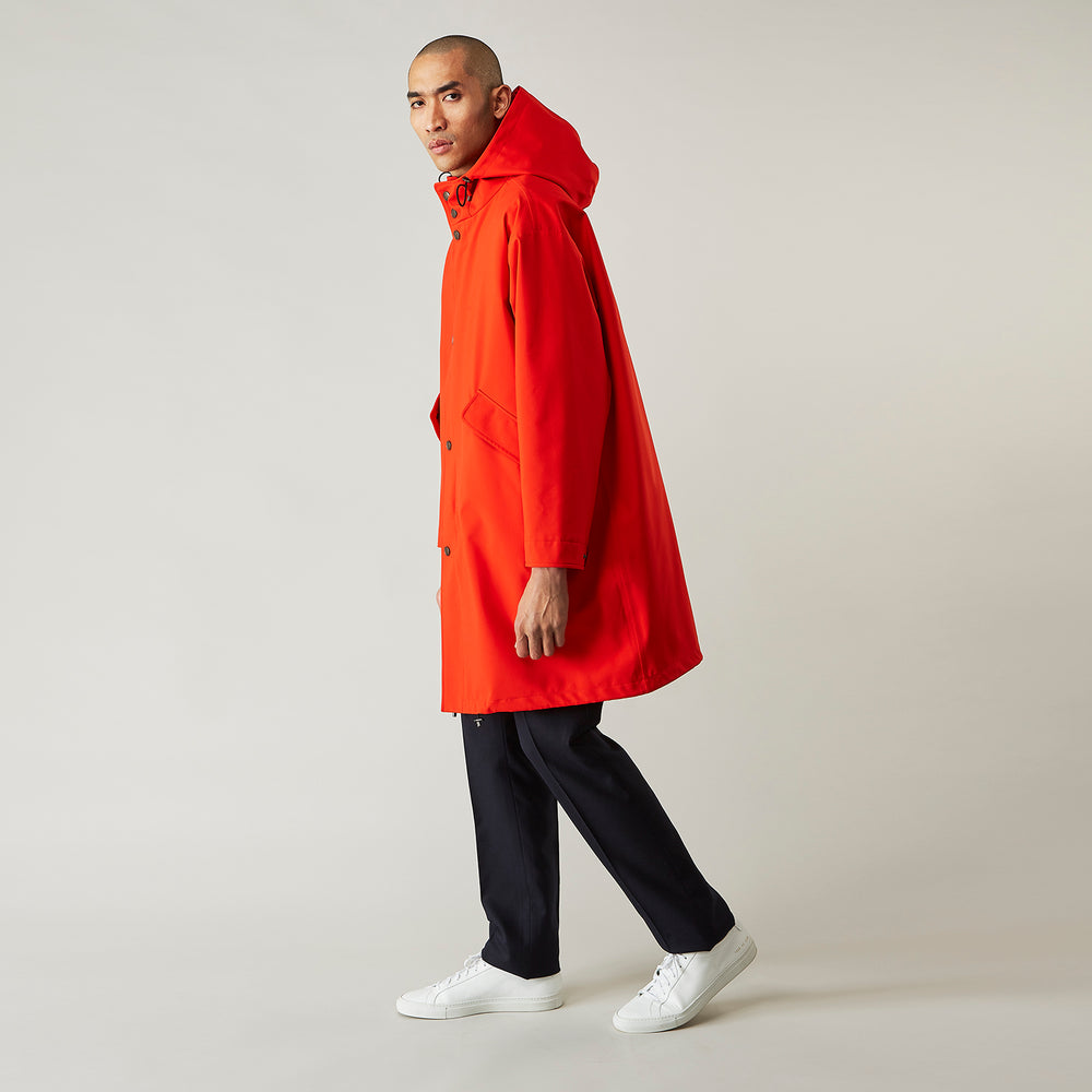 Wearing the Turnbull & Asser Red Walter Sealup Parka with Detachable Liner, black pants, and white sneakers, a person stands in profile against a plain light background—perfect for travel.