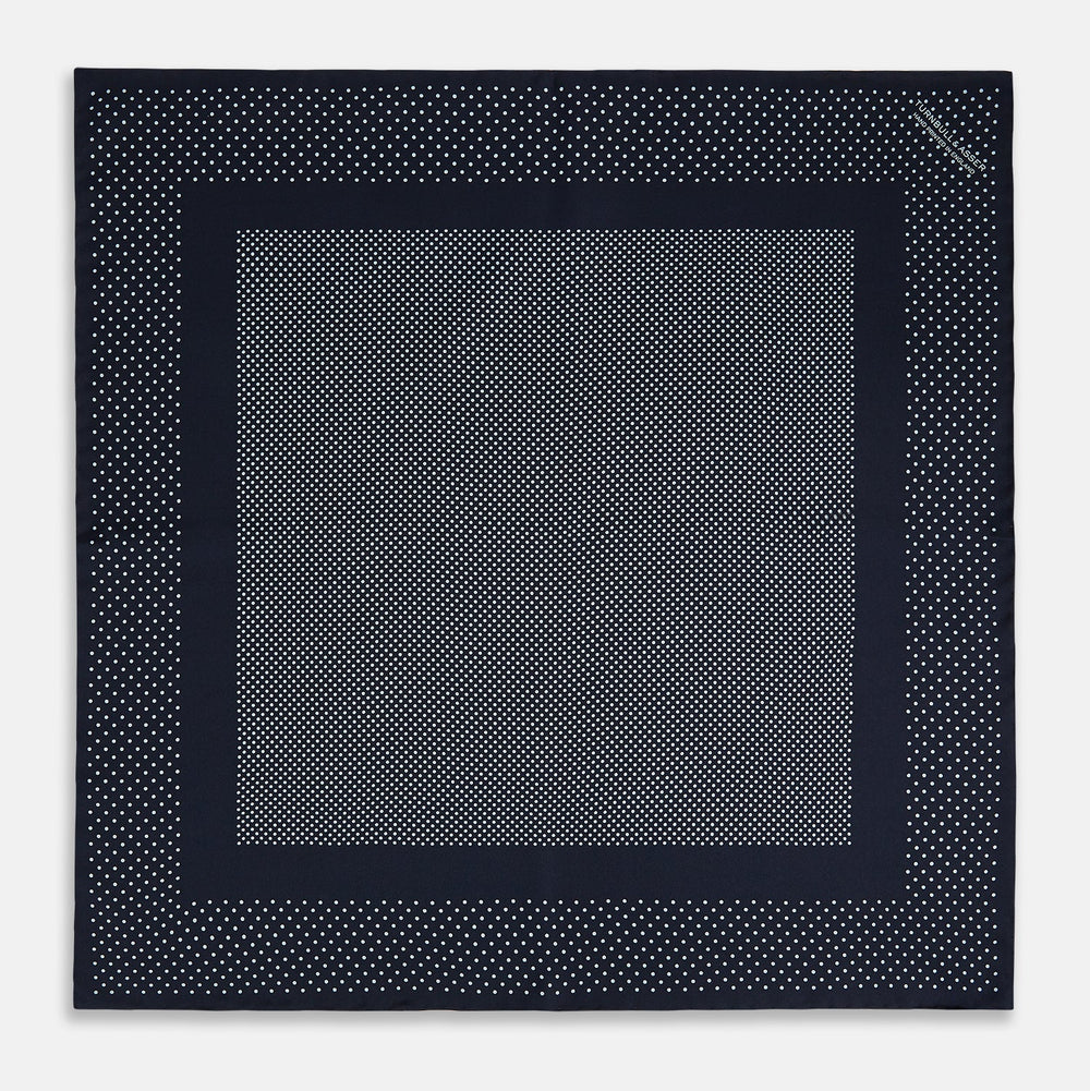 The Turnbull & Asser Navy and Light Blue Dot Silk Pocket Square features white polka dots, a contrasting border, and an inner square design, showcasing handmade craftsmanship with its expertly folded finish.