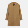 View 2 of product A person wears the Turnbull & Asser Camel Quintern Sealup Raincoat with Detachable Liner, paired with dark pants, standing against a plain light gray background, showing the sleek technical rainwear style with one hand in a pocket.
