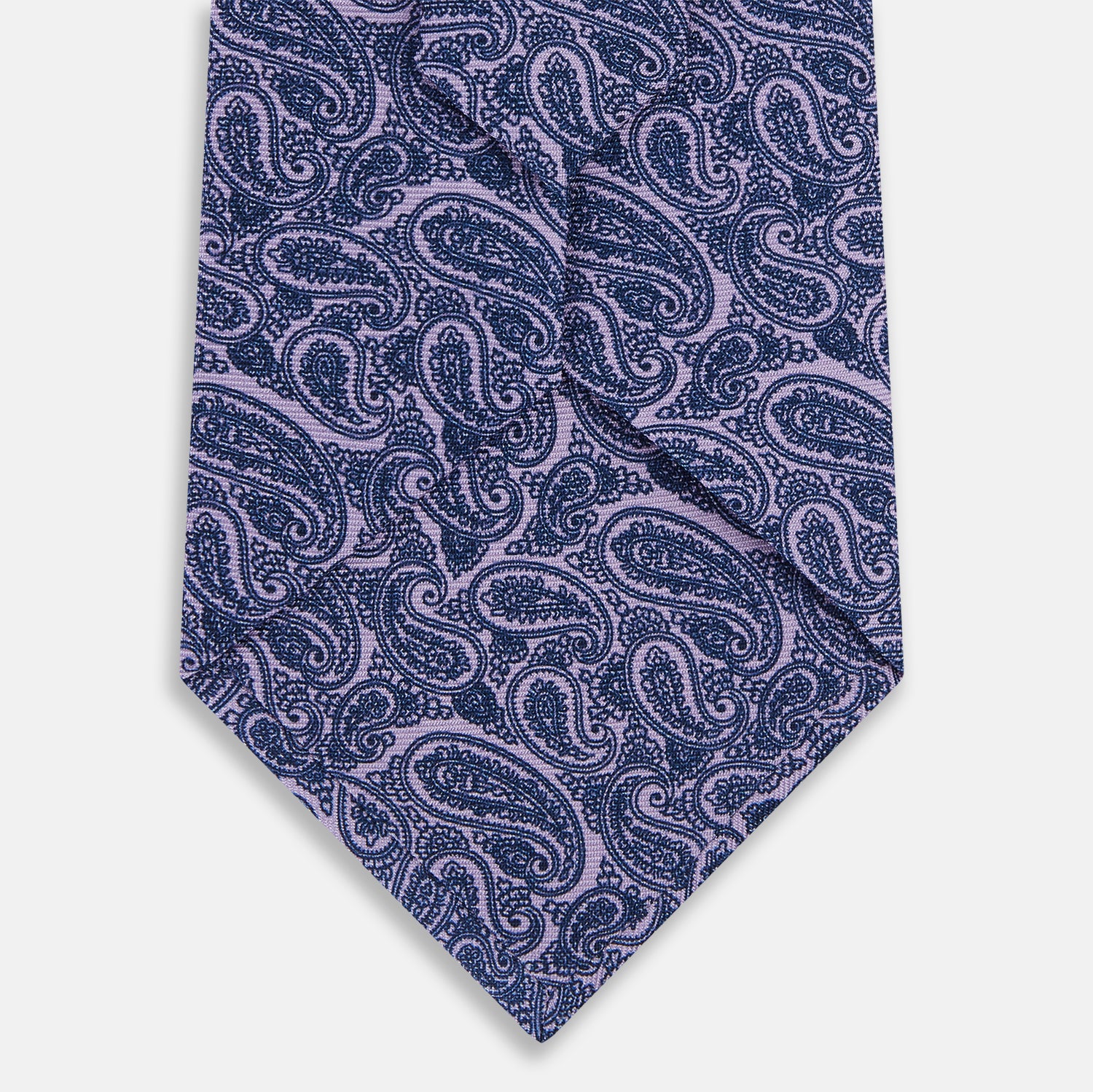 View 3 of product The Turnbull & Asser Lilac Paisley Silk Tie, crafted in England, features a blue paisley pattern on a lilac background and is shown rolled up against a white surface.
