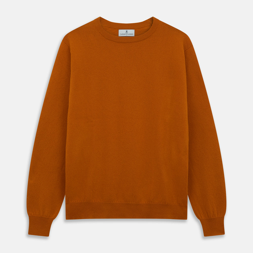 The Turnbull & Asser Rust Glenn Crew Neck Jumper is a plain, long-sleeved Scottish knitwear piece with ribbed cuffs and hem, shown laid flat on a white background.