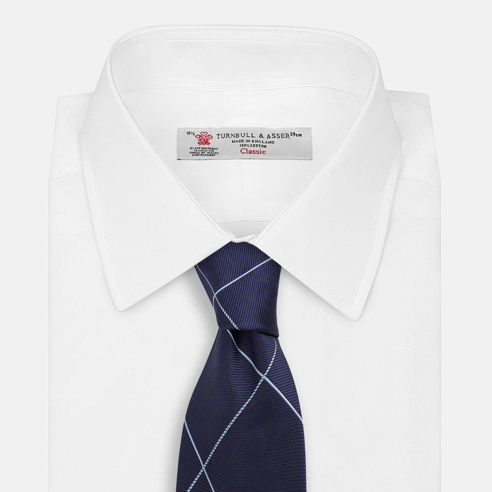 The Turnbull & Asser WINDOW PANE NAVY RIVER TIE features a navy blue base with a subtle light blue check pattern, elegantly rolled on a white background—a sophisticated men's accessory for any wardrobe.