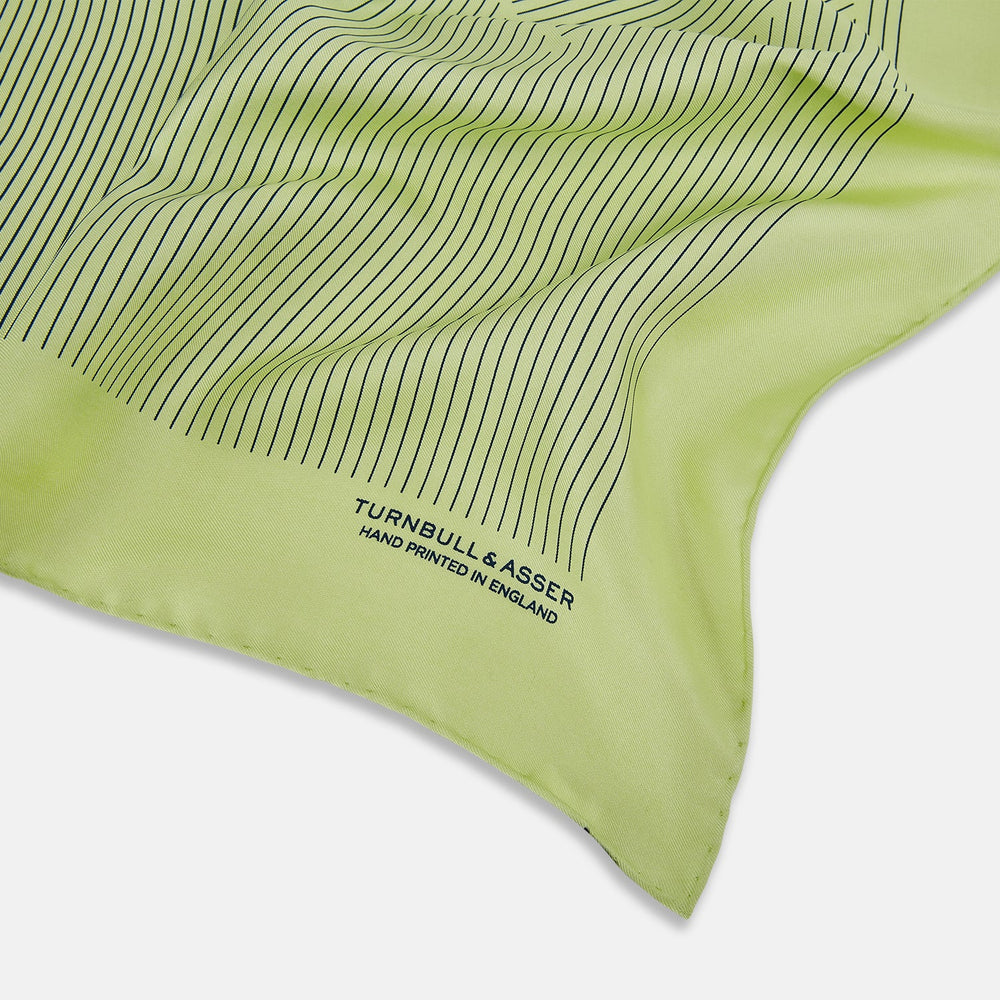 The Melon Green Stripe Silk Pocket Square by Turnbull & Asser features thin vertical black lines on light green silk, neatly folded to display both sides. The lower corner reads “TURNBULL & ASSER HAND PRINTED IN ENGLAND.”.