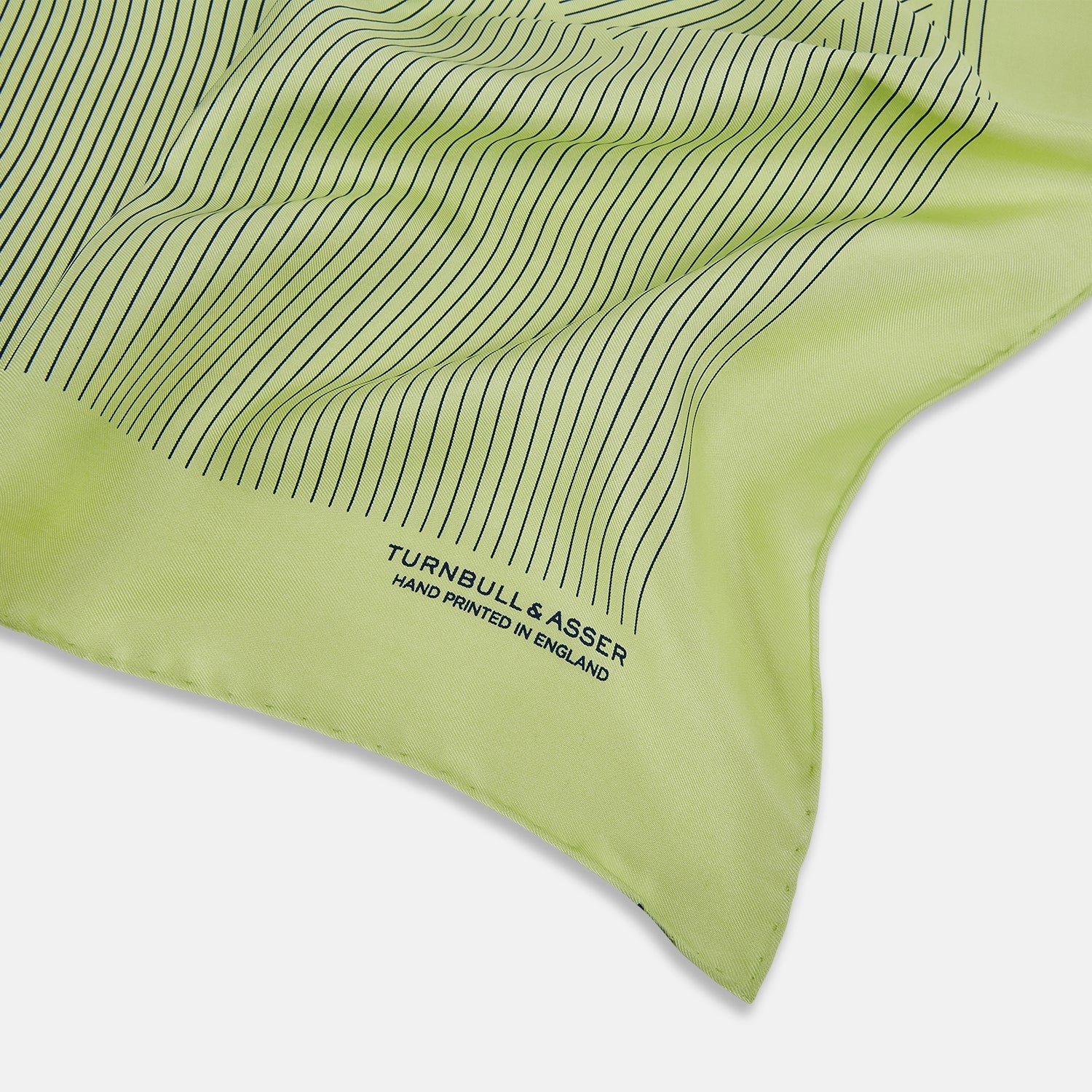 View 2 of product The Melon Green Stripe Silk Pocket Square by Turnbull & Asser features thin vertical black lines on light green silk, neatly folded to display both sides. The lower corner reads “TURNBULL & ASSER HAND PRINTED IN ENGLAND.”.