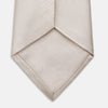 View 4 of product The Turnbull & Asser HORIZONTAL TWILL VELLUM TIE, a light beige silk necktie with a subtle ribbed texture, is shown rolled up on a white background—an essential finishing touch for smart attire.