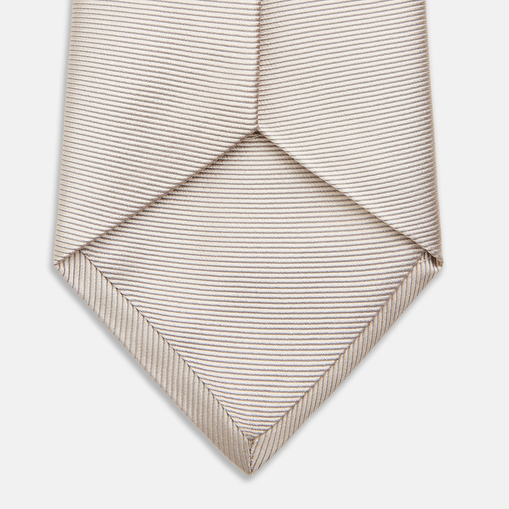 The Turnbull & Asser HORIZONTAL TWILL VELLUM TIE, a light beige silk necktie with a subtle ribbed texture, is shown rolled up on a white background—an essential finishing touch for smart attire.