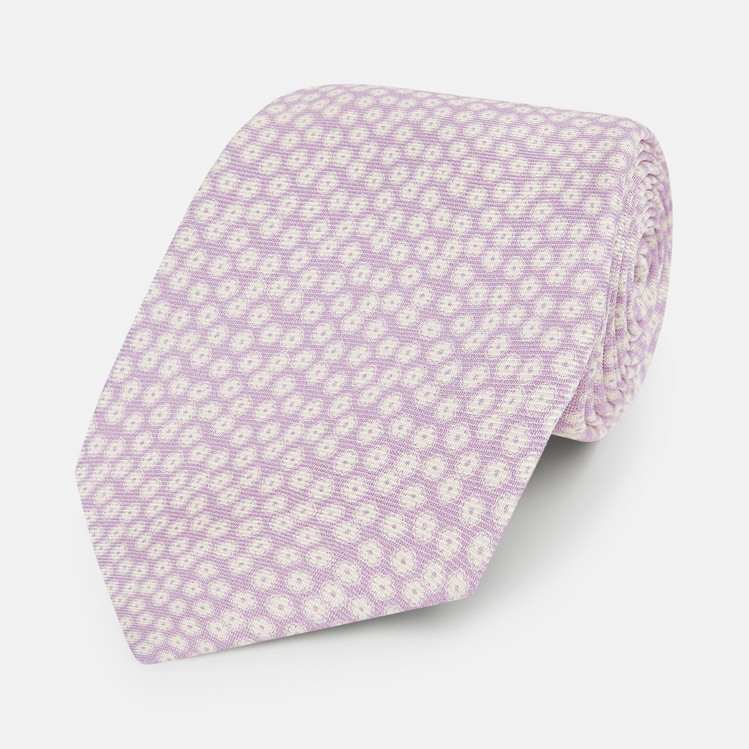 View 1 of product The Turnbull & Asser Lilac Flower Patterned Silk Tie features a light pink hue with a repeating white floral motif, shown rolled up on a plain white background.