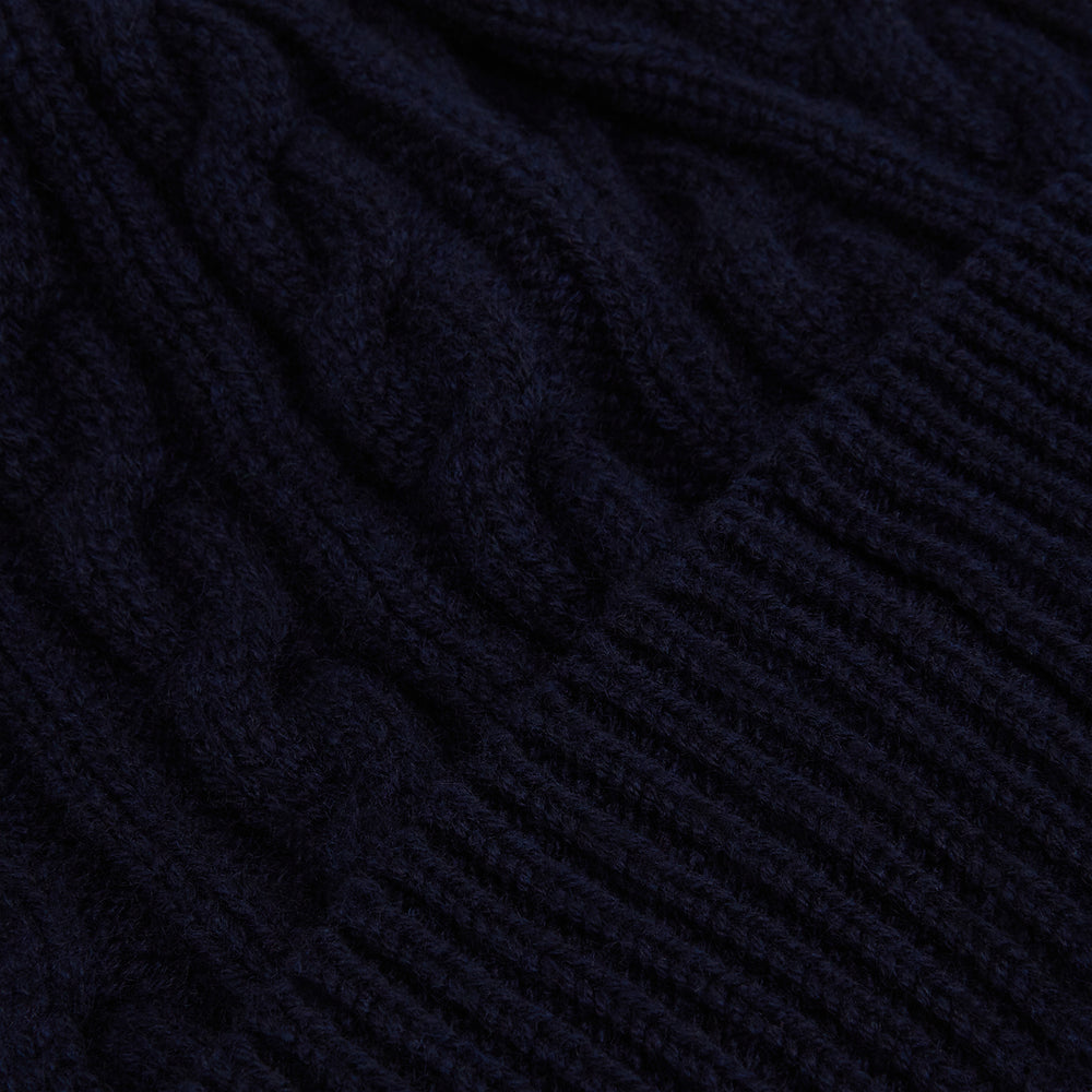 The Turnbull & Asser Midnight Blue Cable Knit Cashmere Beanie features a ribbed folded brim and chunky cable pattern, expertly knitted in England, and shown against a plain white background.
