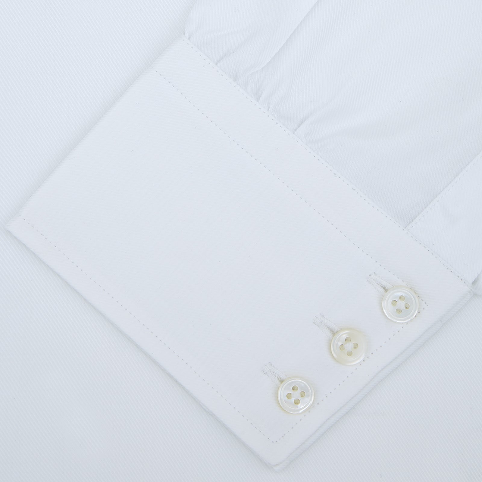 View 4 of product A neatly folded White Sea Island Quality Cotton Twill Shirt by Turnbull & Asser, featuring a T&A collar and 3-button cuffs, is displayed on a light grey background with a label visible inside the collar.