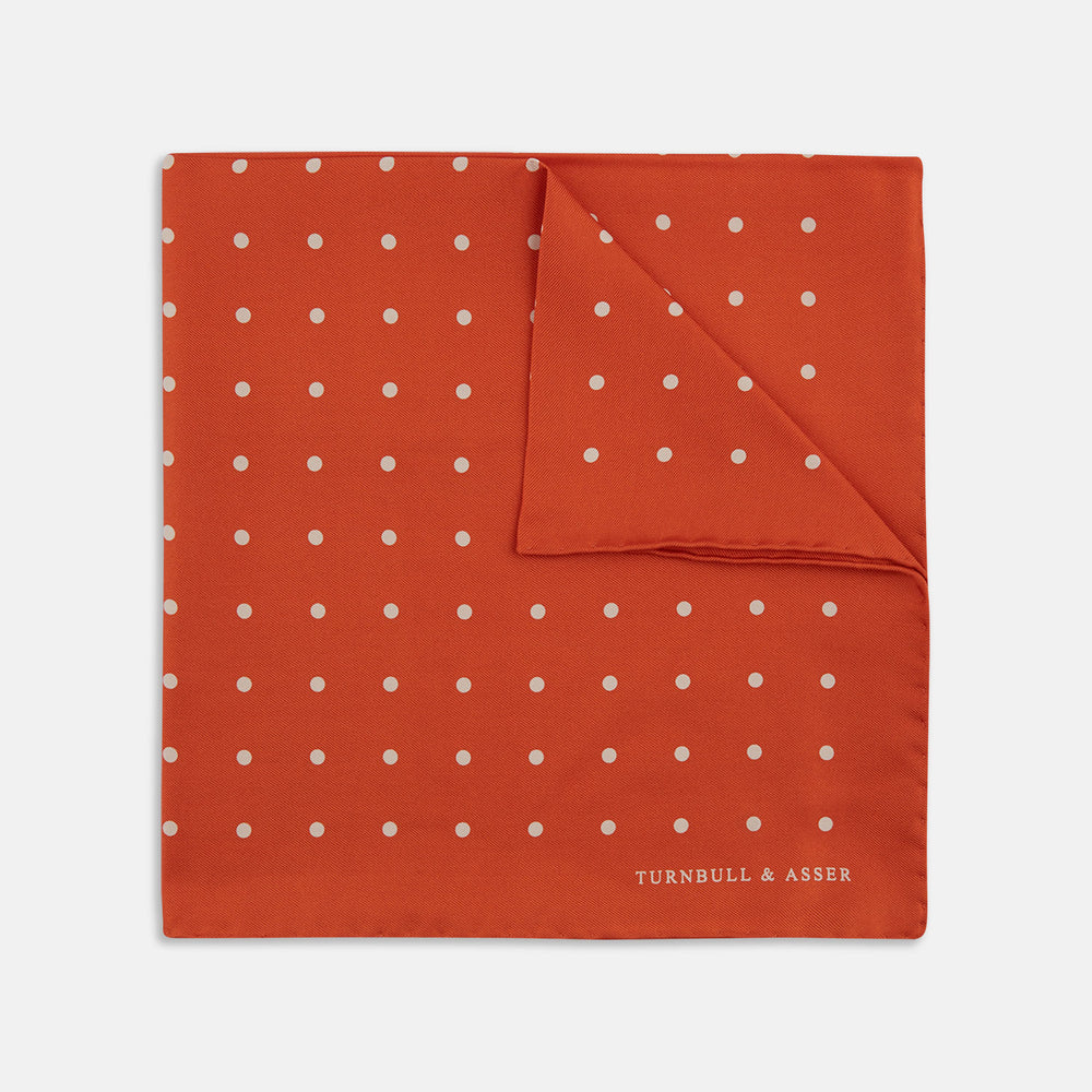 The Orange Spot Silk Pocket Square by Turnbull & Asser features evenly spaced white polka dots and the brand’s name in one corner, making this dapper accessory a standout addition to any outfit.