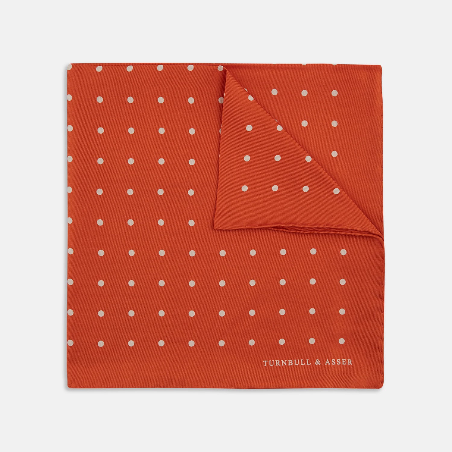 View 1 of product The Orange Spot Silk Pocket Square by Turnbull & Asser features evenly spaced white polka dots and the brand’s name in one corner, making this dapper accessory a standout addition to any outfit.