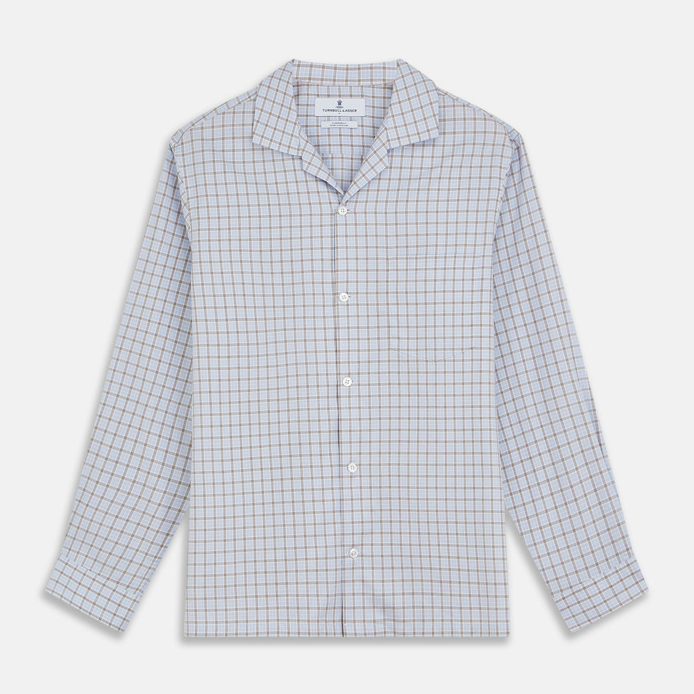 A man wearing glasses and a Pale Blue Multi Check Cashmerello Holiday Fit Winnington Shirt by Turnbull & Asser leans casually against a white countertop, looking at the camera with a neutral expression.