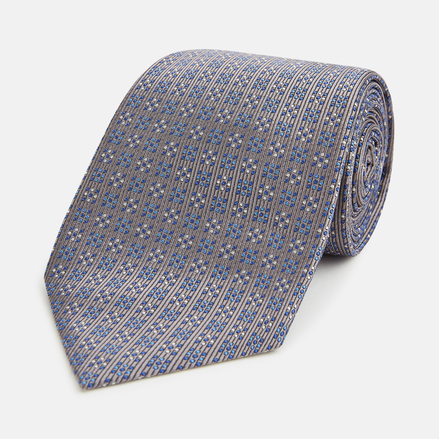 View 1 of product The Turnbull & Asser Silver and Pale Blue Multi Dot Silk Tie features elegant small dots on light brown silk, ideal for modern office wear, shown rolled up against a white background.