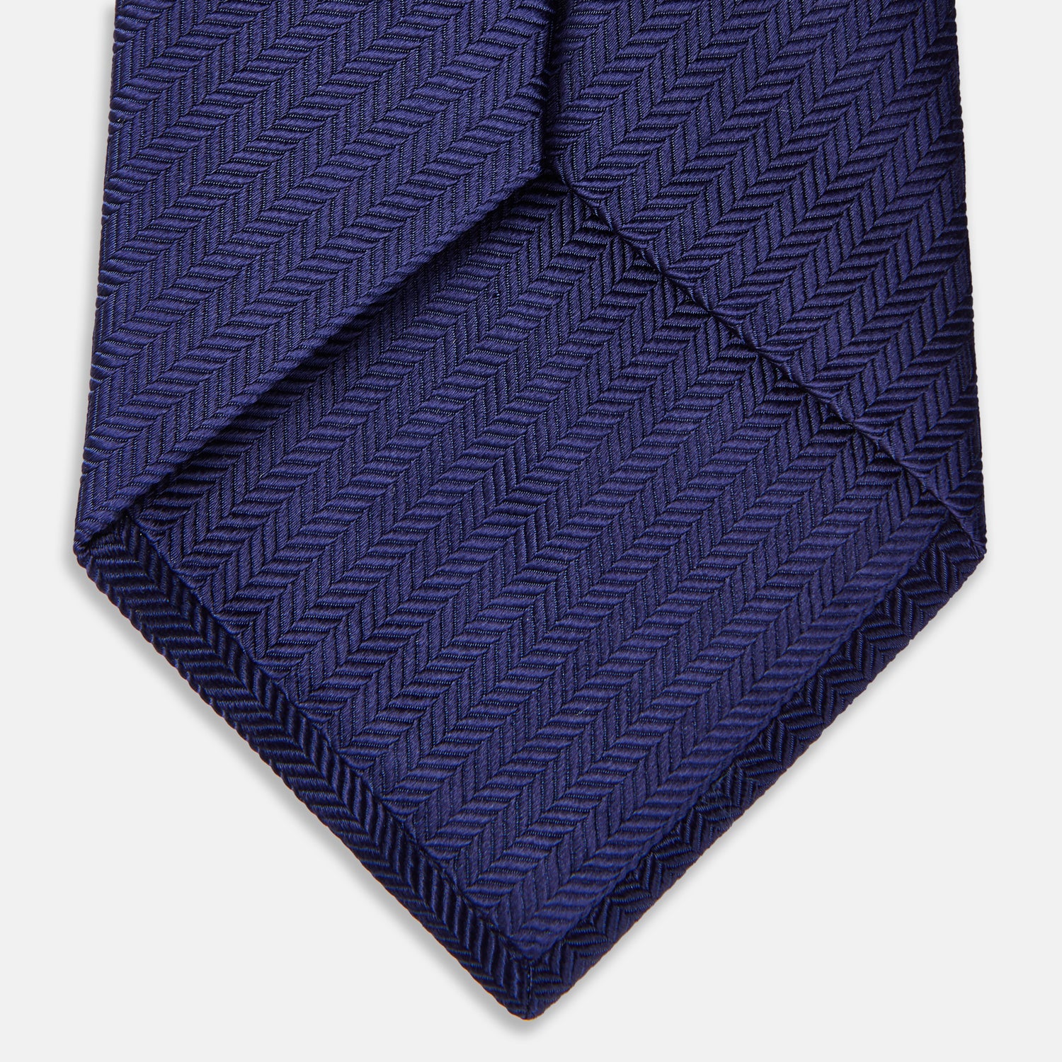 View 3 of product The PLAIN HERRINGBONE NAVY TIE by Turnbull & Asser, crafted from silk with a subtle pattern, is elegantly rolled and displayed against a plain white background.