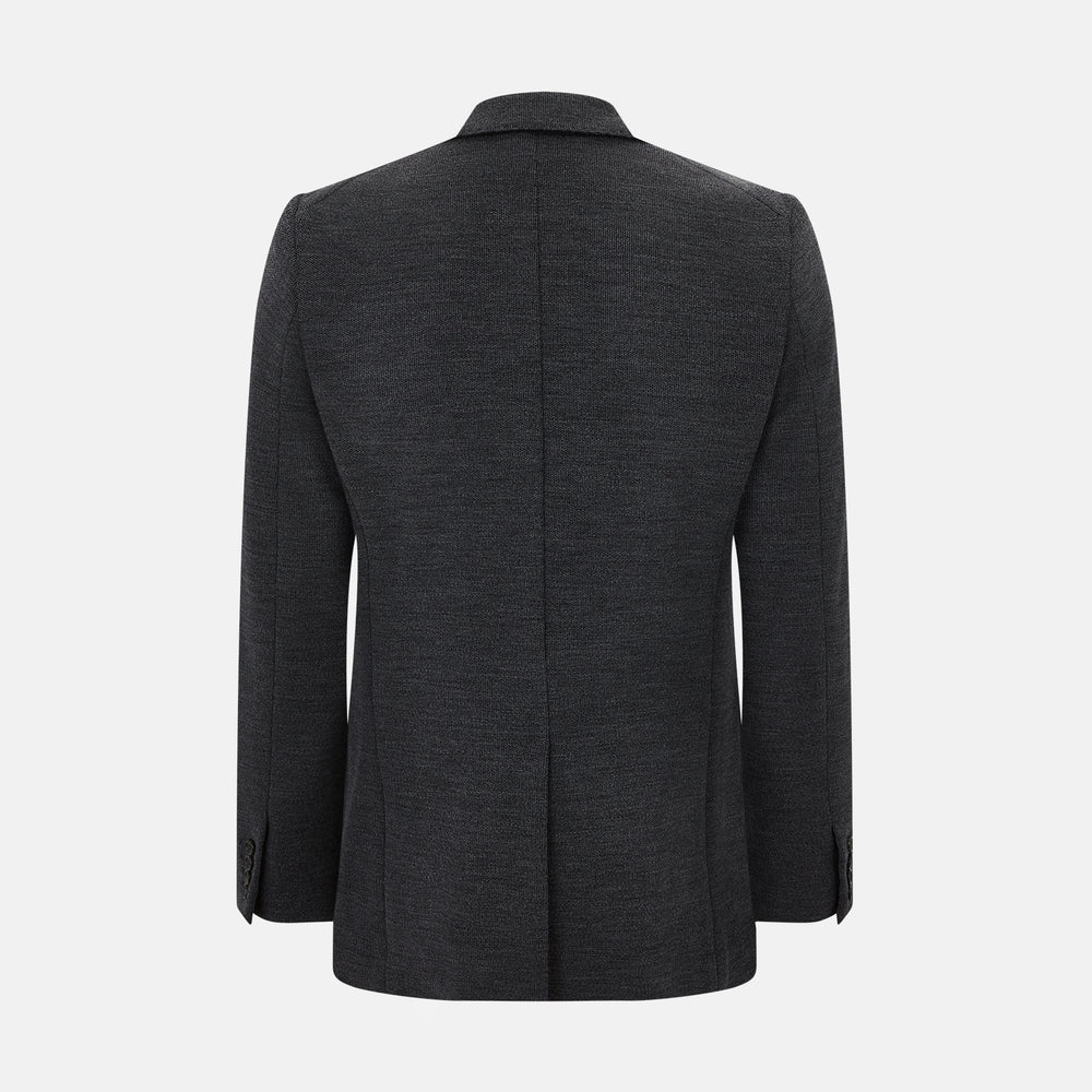 The Turnbull & Asser Graphite Knitted Oxford Blazer for men features a dark gray hue, two buttons, notched lapels, and three front pockets—a modern British-inspired piece styled elegantly against a light background.