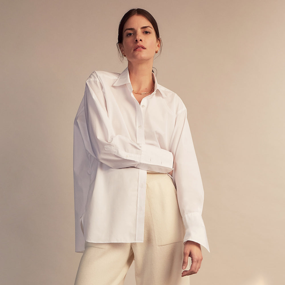 A woman with straight brown hair pulled back wears the Turnbull & Asser White Cotton Marlene Shirt, featuring classic menswear details, paired with high-waisted cream trousers against a neutral background.