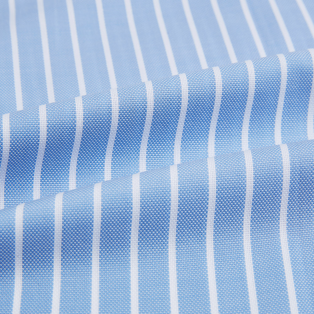 The Turnbull & Asser Sky Blue Wide Pinstripe Mayfair Shirt features long sleeves, a classic collar, and buttoned cuffs, laid flat against a white background for a refined formal look.