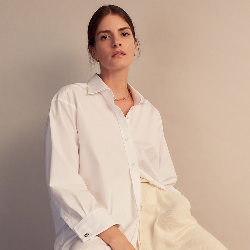 A woman with straight brown hair pulled back wears the Turnbull & Asser White Cotton Marlene Shirt, featuring classic menswear details, paired with high-waisted cream trousers against a neutral background.