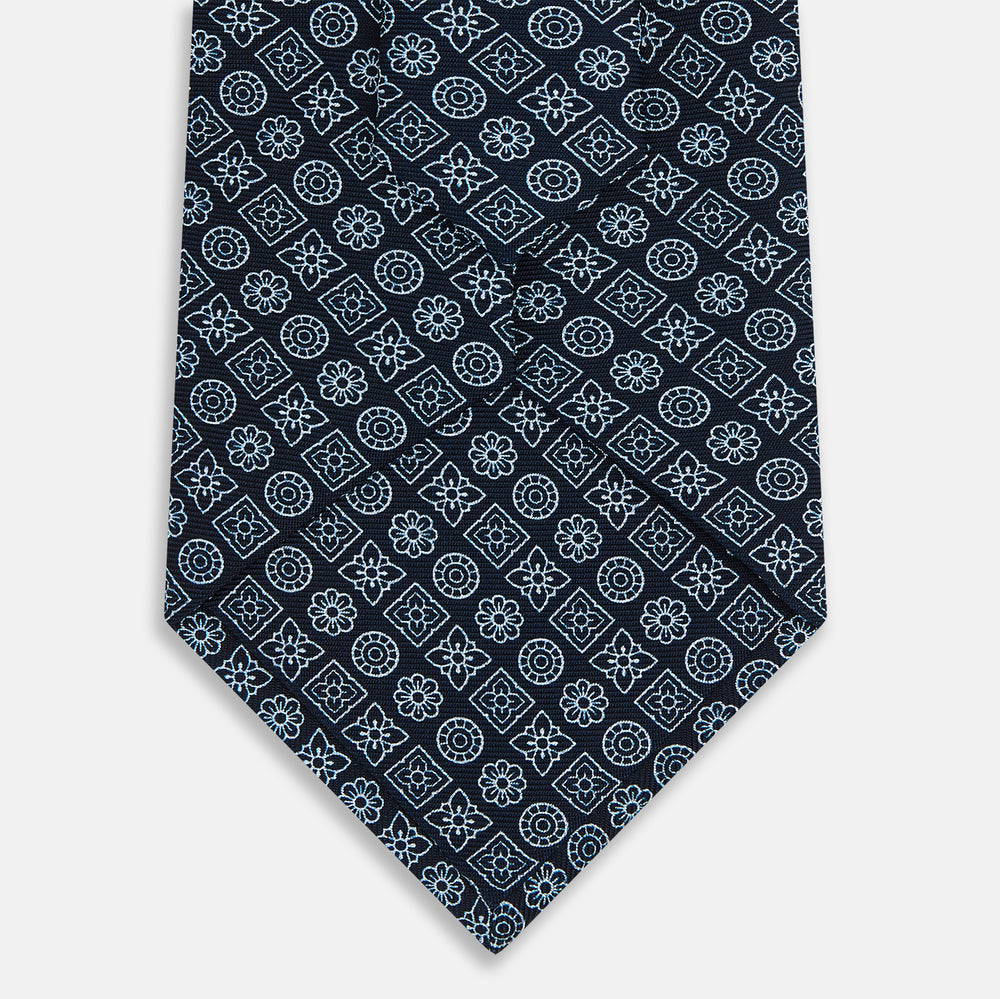 The Turnbull & Asser Navy Floral Tile Pattern Printed Silk Tie features light blue geometric and floral motifs in a diamond grid, elegantly displayed and crafted from fine English silk.