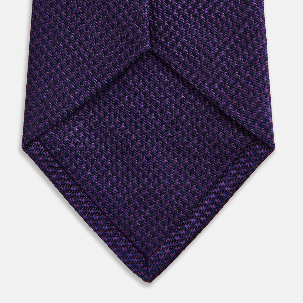 The HOUNDSTOOTH NAVY PLUM TIE by Turnbull & Asser, featuring a textured pattern, is showcased rolled up against a plain white background—an essential accessory.