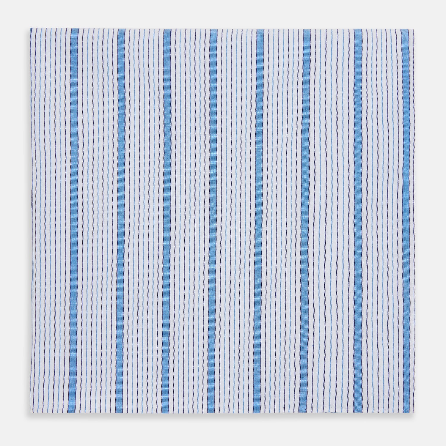 View 1 of product The Hand Rolled Blue Multi Track Stripe Handkerchief by Turnbull & Asser features a square white design with vertical light blue and navy stripes of varying widths—a timeless gentleman’s accessory.