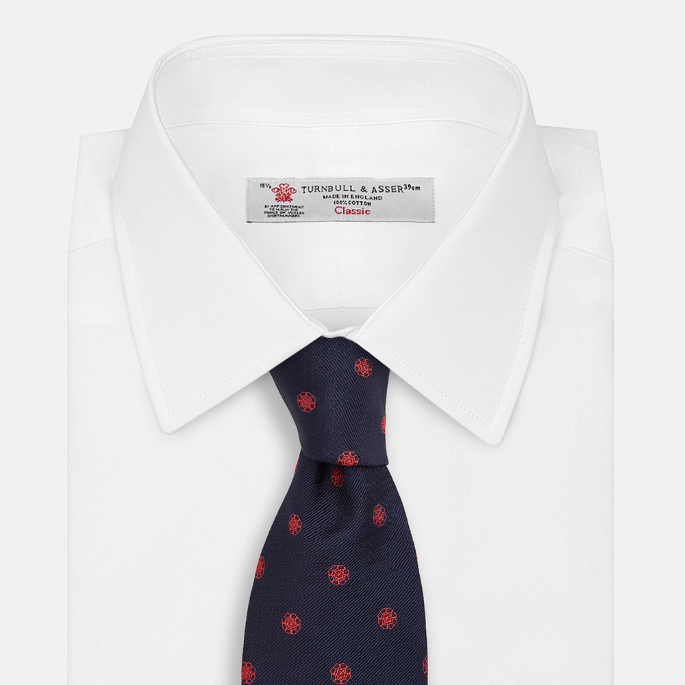 The EMBLEM SPOT NAVY TULIP TIE by Turnbull & Asser features a navy base with red circle motifs, neatly rolled on a white background—an essential accessory for refined style.