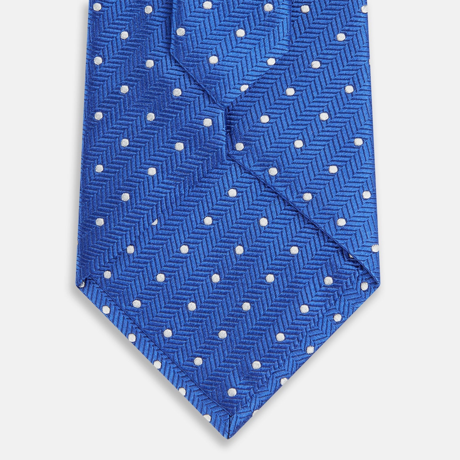 View 3 of product The Turnbull & Asser Blue and White Micro Dot Silk Tie features a subtle herringbone pattern with small white dots, ideal for modern office attire, and is shown rolled up on a white background.