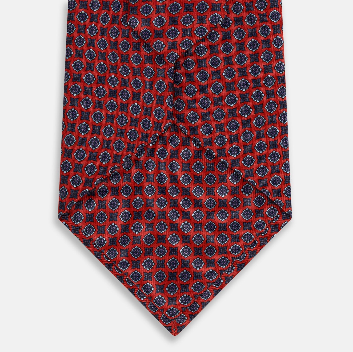 View 3 of product The Turnbull & Asser Red and Blue Geometric Floral Silk Tie features a red background with small blue and white circular floral patterns, exemplifying British craftsmanship.