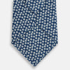 View 3 of product The Turnbull & Asser Azzurro Flower Patterned Silk Tie features a repeating motif of small white flowers with dark centers on blue silk, rolled up and displayed against a plain white background.