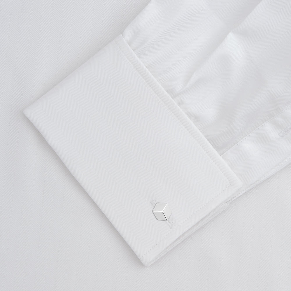 The Turnbull & Asser White Herringbone Sea Island Quality Cotton Shirt features a T&A collar, double cuffs, and chest pocket. Crafted for luxury with a classic design, it’s shown neatly folded against a light grey background—ideal for evening wear.