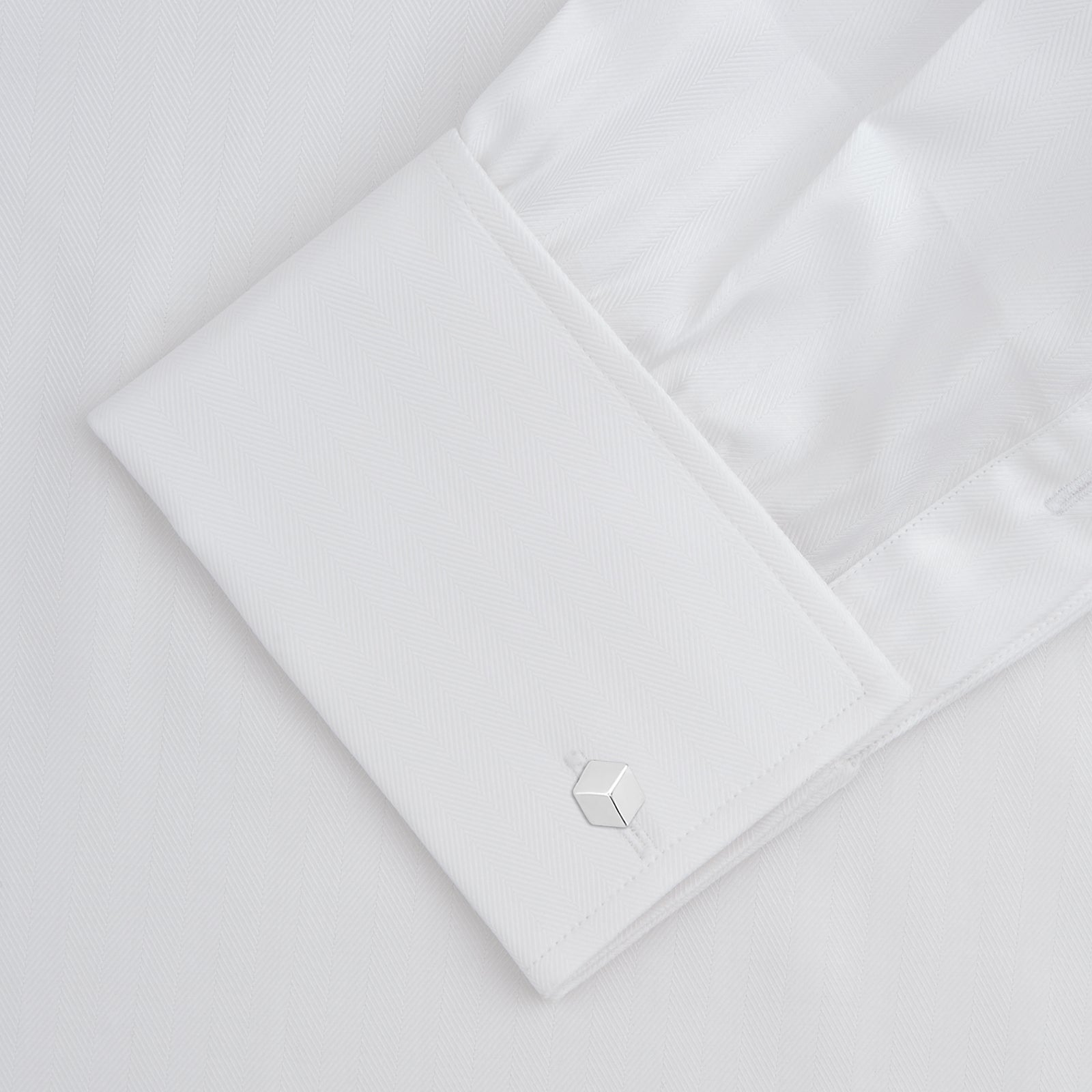 View 4 of product The Turnbull & Asser White Herringbone Sea Island Quality Cotton Shirt features a T&A collar, double cuffs, and chest pocket. Crafted for luxury with a classic design, it’s shown neatly folded against a light grey background—ideal for evening wear.
