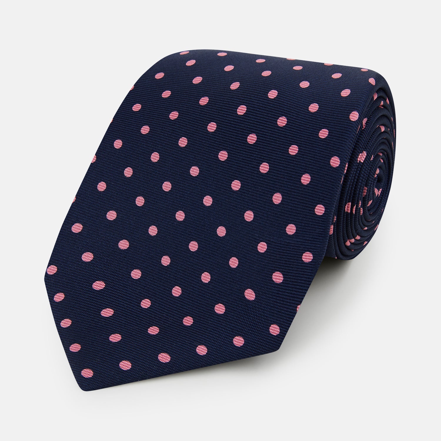 View 1 of product The Pink Dot and Navy Silk Tie by Turnbull & Asser features evenly spaced pink polka dots on navy silk, rolled neatly on a white background—a classic British style ideal for refined occasions.
