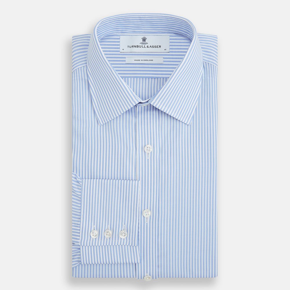 The Turnbull & Asser Blue Bengal Stripe Mayfair Shirt features light blue and white vertical stripes, a classic T&A collar, white buttons, and buttoned cuffs. Laid flat on a white background.