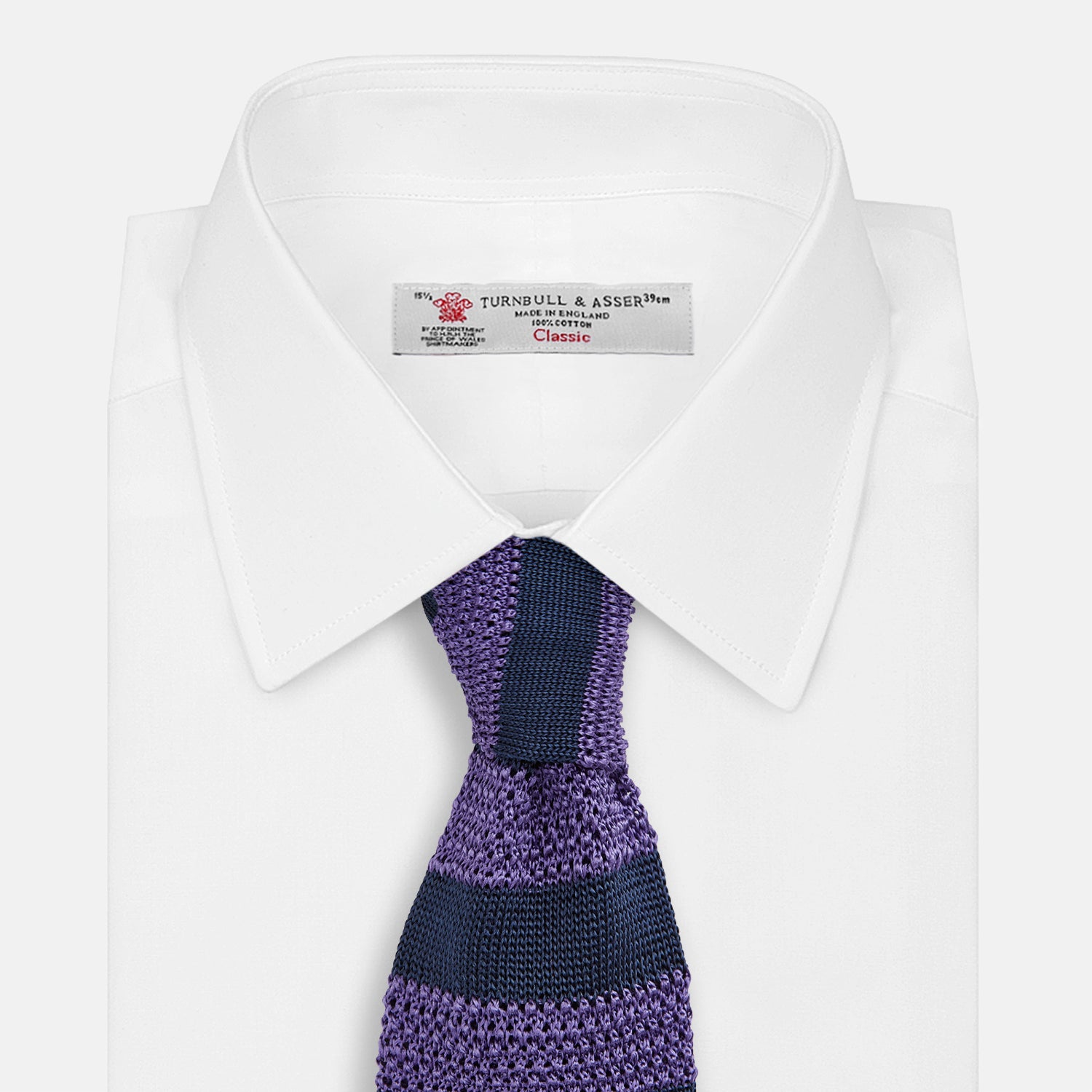 View 2 of product The KNITTED STRIPE PURPLE TIE by Turnbull & Asser features bold dark blue and purple stripes, making it an essential smart accessory. Shown rolled up on a white background.