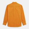 View 8 of product A man stands against a tan background, wearing a Turnbull & Asser Orange Weekend Fit Cotton & Wool Shirt with Derby Collar and 1 Button Cuffs, tucked into dark blue dress pants with a black belt and shoes. He has one hand in his pocket.