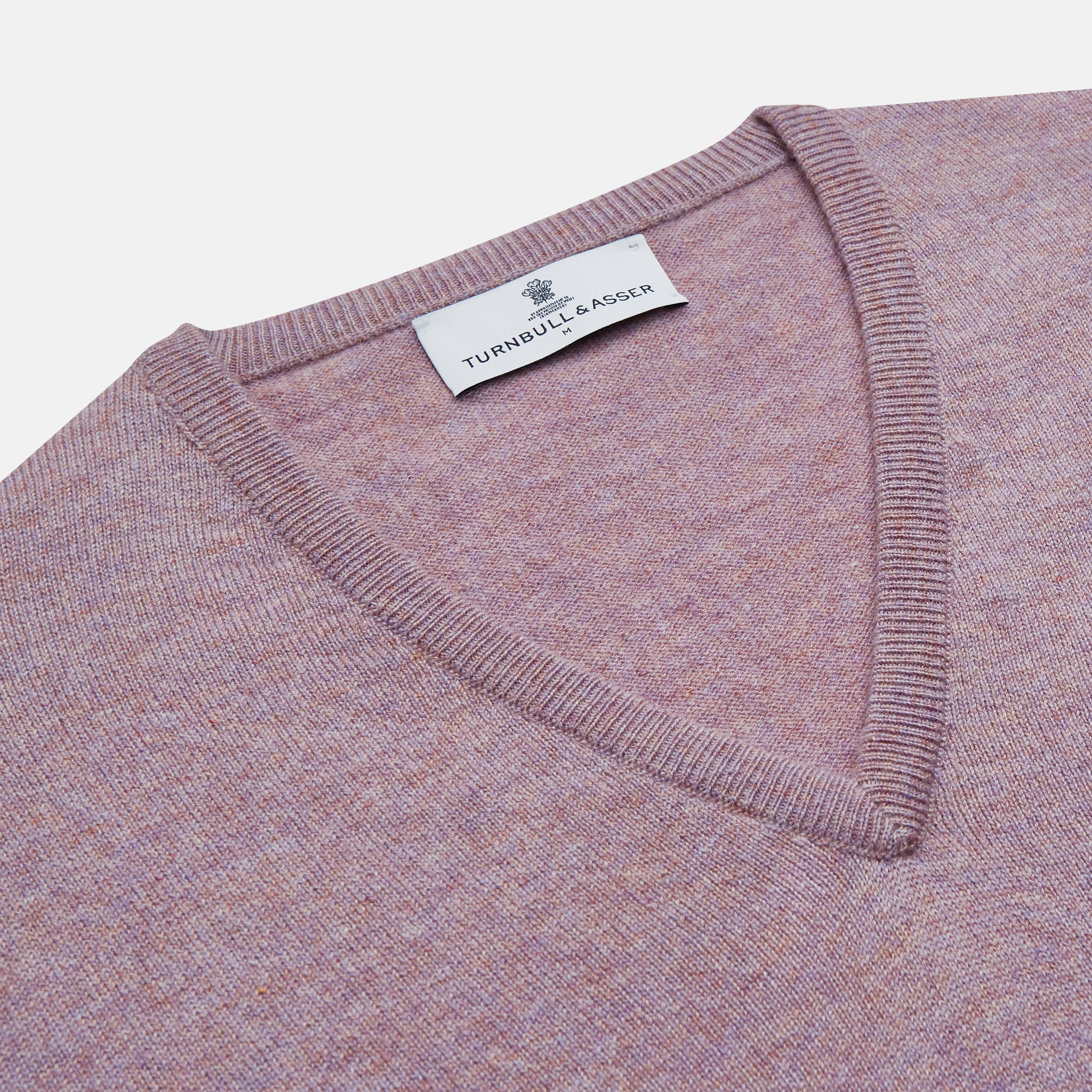 View 2 of product The Turnbull & Asser Lilac Heather Paden Cashmere V-Neck Jumper is laid flat on a white background, showcasing its light purple hue, ribbed cuffs and hem, long sleeves, and soft heathered texture.