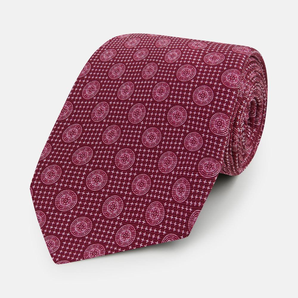 The Turnbull & Asser Burgundy Medallion Silk Tie features a geometric pattern of small circles intersected by diagonal pink lines, elegantly displayed against a white background.